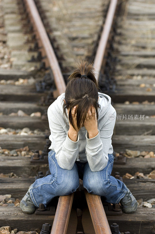 女孩坐在铁轨上， 双手捂着脸